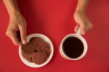 Woman holding a white Cup of coffee. concept-Warmth and comfort in the house. Chocolate cookies are on the plate. red background. flat lay. the view from the top.