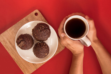 Woman holding a white Cup of coffee. concept-Warmth and comfort in the house. Chocolate cupcakes are on the plate. red background. flat lay. the view from the top.