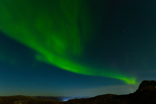 Northern lights, aurora in the sky above the hills and rocks at night. © Moroshka