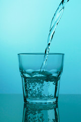 Water is poured into a glass on a blue background, close-up