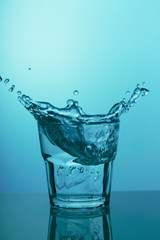 Glass with clear water and splashes on blue background