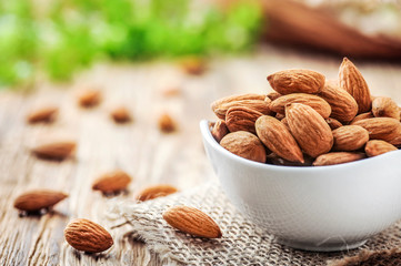 Almonds in white porcelain bowl on wooden table. Almond concept with copyspace.