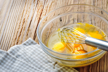 Whipped eggs. Woman whisking fresh eggs in glass bowl on wooden table.