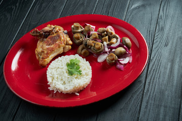 Close up on Boiled rice with pickled mushrooms and chicken on a red plate on a black wooden background. Healthy food for diet
