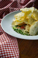 Caesar salad with croutons, lettuce, olives and chicken in a white bowl on a rustic wooden background with tablecloth. Selective, soft focus