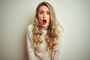 Beautiful woman wearing winter turtleneck sweater over isolated white background In shock face, looking skeptical and sarcastic, surprised with open mouth