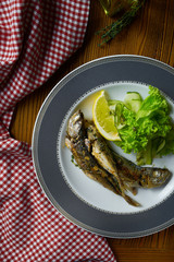 Close up Grilled fish sprat with salad on white plate in composition with red cloth on wooden table. Food photo background. Seafood