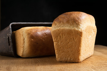 Two loaves of white bread on an oak board