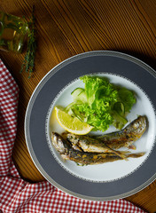 Close up Grilled fish sprat with salad on white plate in composition with red cloth on wooden table. Food photo background. Seafood
