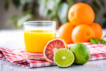 Orange juice in glass on white table with tropical fruits like a orange, lime red orange. Orange