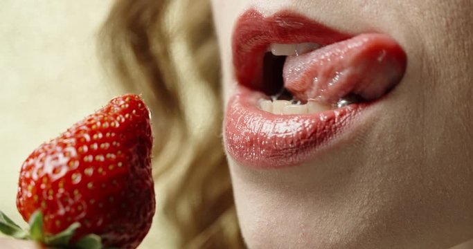 Extreme close up shot of sexy woman with red lipstick applied on lips and with pierced tongue eating strawberry slow motion 4k footage