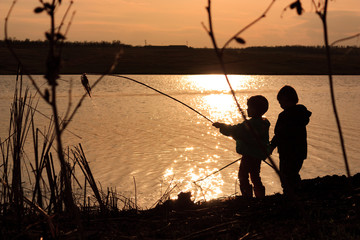 Children play on the river bank at sunset.