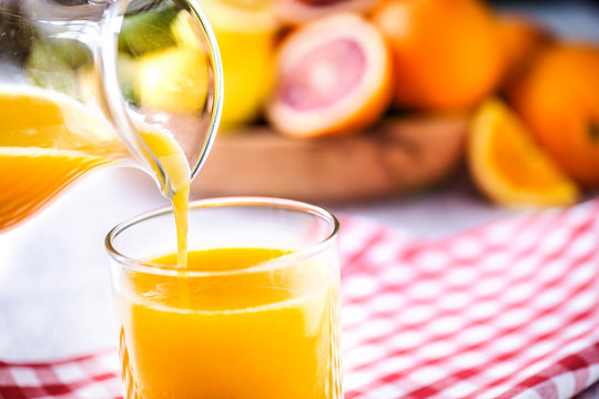 Pouring orange juice in to glass. Tropical fruits juice in glass with orange, lime and grep. Fresh orange nectar.