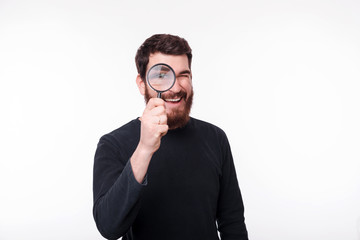 Handsome bearded man watching you through a magnifying glass on white background.