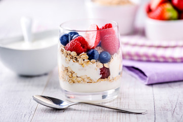 Fresh yoghurt with forest fruits in clear glass. Blueberries, raspberries in white bowl. Healthy morning breakfast.