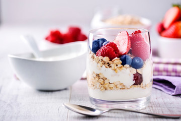 Fresh yoghurt with forest fruits in clear glass. Blueberries, raspberries in white bowl. Healthy morning breakfast.