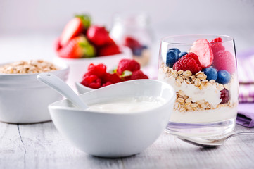 Fresh yoghurt with forest fruits in clear glass. Blueberries, raspberries in white bowl. Healthy morning breakfast.