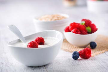 Fresh white yoghurt with raw forest fruits. Rasberries in white yoghurt in bowl on white table. Best meal for healthy breakfast.