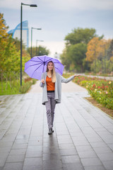 Young beautiful girl walks in the autumn under an umbrella and checks with her hand whether it is raining