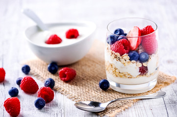 Yoghurt with forest fruits in glass.  Fresh morning healty breakfast. Raspberries, blueberries on white table.