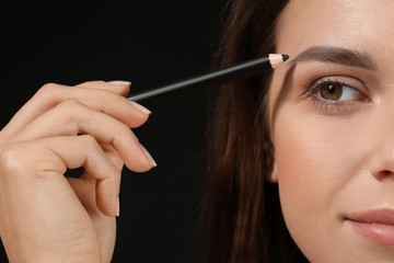 Obraz premium Beautiful young woman with pencil for eyebrows on dark background, closeup