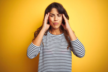 Young beautiful woman wearing stripes t-shirt standing over yelllow isolated background with hand on head for pain in head because stress. Suffering migraine.