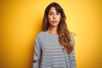 Young beautiful woman wearing stripes t-shirt standing over yelllow isolated background Relaxed...