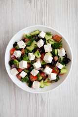 Homemade Shepherd's salad with cucumbers, feta and parsley in a white bowl on a white wooden background, top view.