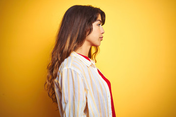 Young beautiful woman wearing red t-shirt and stripes shirt over yellow isolated background looking to side, relax profile pose with natural face with confident smile.