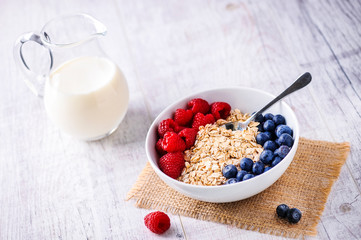 Oat flakeswith forest fruits in white plate on rustic table with jar of milk in backgrund.