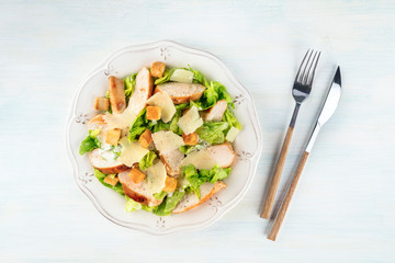 Chicken Caesar salad. Slices of chicken breast, green lettuce, Parmesan cheese, and croutons, shot from the top with a fork and knife
