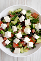 Homemade Shepherd's salad with cucumbers, feta and parsley in a white bowl on a white wooden surface, top view. From above, overhead.