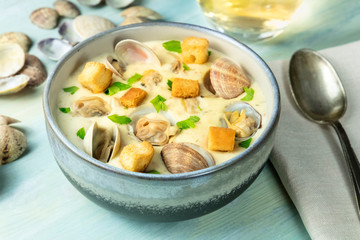 Clam chowder with fresh parsley and croutons, with shells and a glass of white wine on a blue background