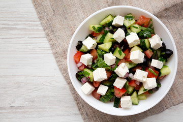 Homemade Shepherd's salad with cucumbers, feta and parsley in a white bowl on a white wooden table, top view. From above, overhead. Copy space.