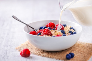 Pouring fresh milk in to oat flakes with forest fruits.