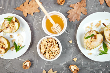 Tasty roast pears with honey and walnuts on white plates on grey background table. Top view.  Flat lay. Copy space.