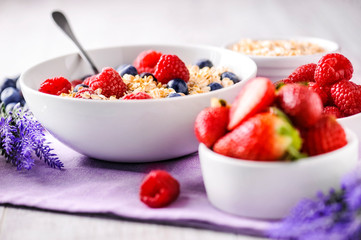 Oat flakes with fresh fruits in white plate. Strawberries, raspberries and blueberries on white table. Lavender flowers.