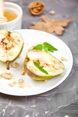 Tasty roast pears with honey and walnuts on white plates on grey background table.