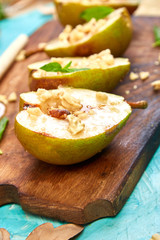 Tasty roast pears with honey and walnuts on wooden board on blue background table.