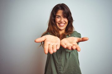 Young beautiful woman wearing green shirt standing over grey isolated background Smiling with hands palms together receiving or giving gesture. Hold and protection