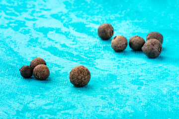 A close-up of allspice, Jamaica pepper, peppercorns on a vibrant turquoise blue background with a...