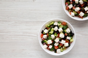 Homemade Shepherd's salad with cucumbers, feta and parsley in white bowls on a white wooden table,...