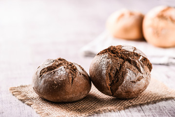 Dark tasty rolls bread on white table. Finest dark baked buns.
