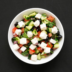 Homemade Shepherd's salad with cucumbers, feta and parsley in a white bowl on a black background, top view. From above, overhead, flat lay. Close-up.