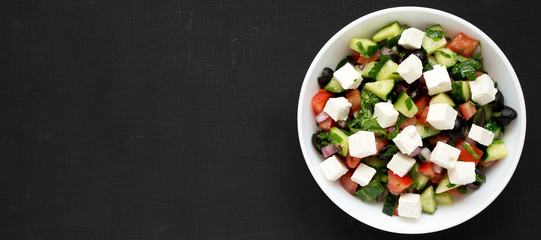Homemade Shepherd's salad with cucumbers, feta and parsley in a white bowl on a black surface, top...