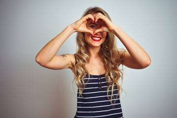 Young beautiful woman wearing stripes t-shirt standing over white isolated background Doing heart shape with hand and fingers smiling looking through sign