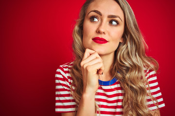 Young beautiful woman wearing stripes t-shirt standing over red isolated background serious face thinking about question, very confused idea