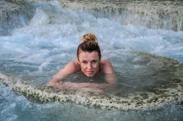 Young charming girl bathes in the healing thermal mineral springs in the resort of Saturnia Italy