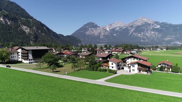 Aerial bird view footage of typical Austrian homes located at the Zillertal in Austria vehicle driving by also Alps mountain range showing in far background while camera is panning right 4k quality