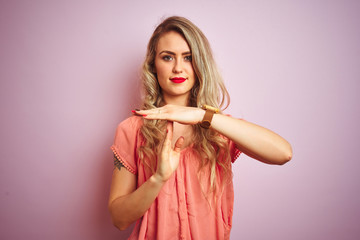 Young beautiful woman wearing t-shirt standing over pink isolated background Doing time out gesture...